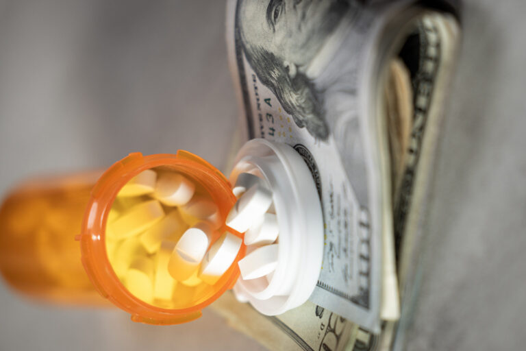 A visually impactful shot featuring prescription pill bottles and scattered US dollar bills (cash). This image symbolizes the high cost and financial burden of medication and the debt caused by healthcare expenses in the USA.