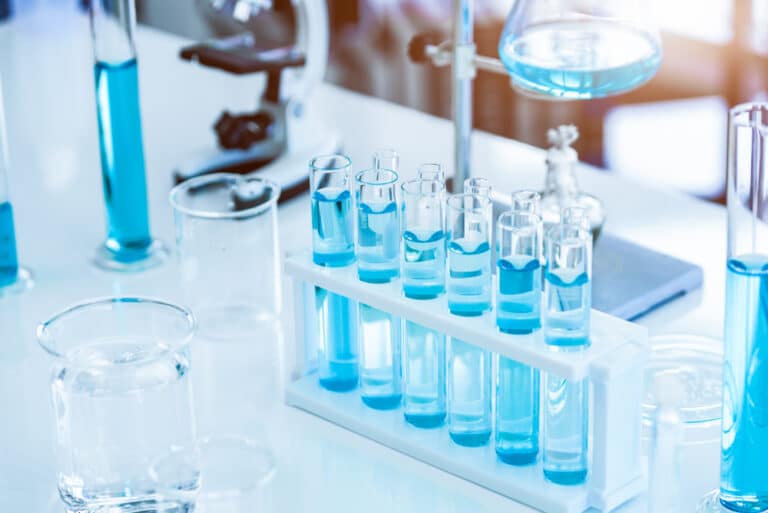 Pharmaceutical test tubes with blue liquid in a lab, illustrating biosimilar drug development and pathways to improved access and cost savings.