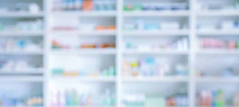 Blurred view of a pharmacy medication storage area illustrating consumer experiences with accessing and affording GLP‑1 treatments.